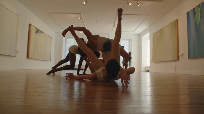 Une danseuse en mouvement devant un tableau, dans une salle de musée