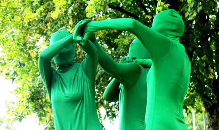 Trois danseurs en combinaison verte enlacés sous les arbres d’un parc