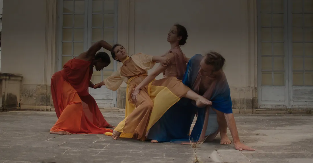 Quatre danseurs de la Compagnie NAO en costumes rouge, jaune et bleu, devant une façade de pierre